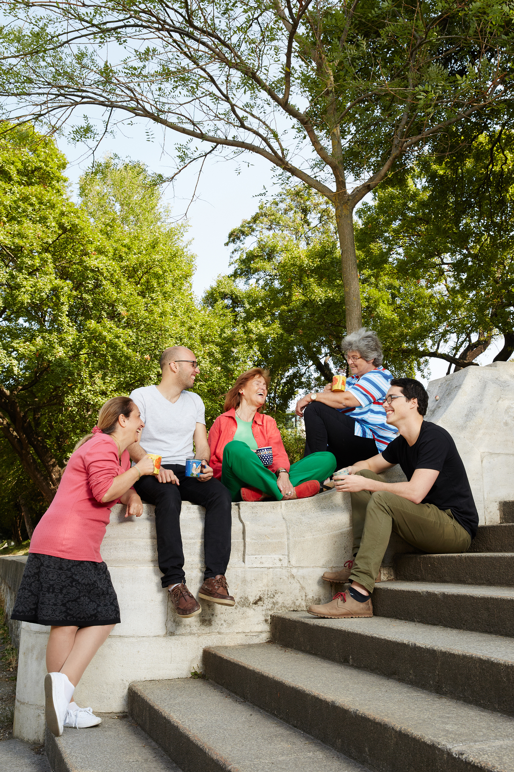 5 Frauen und Männer plaudern mit bunten Kaffeetassen im Park
