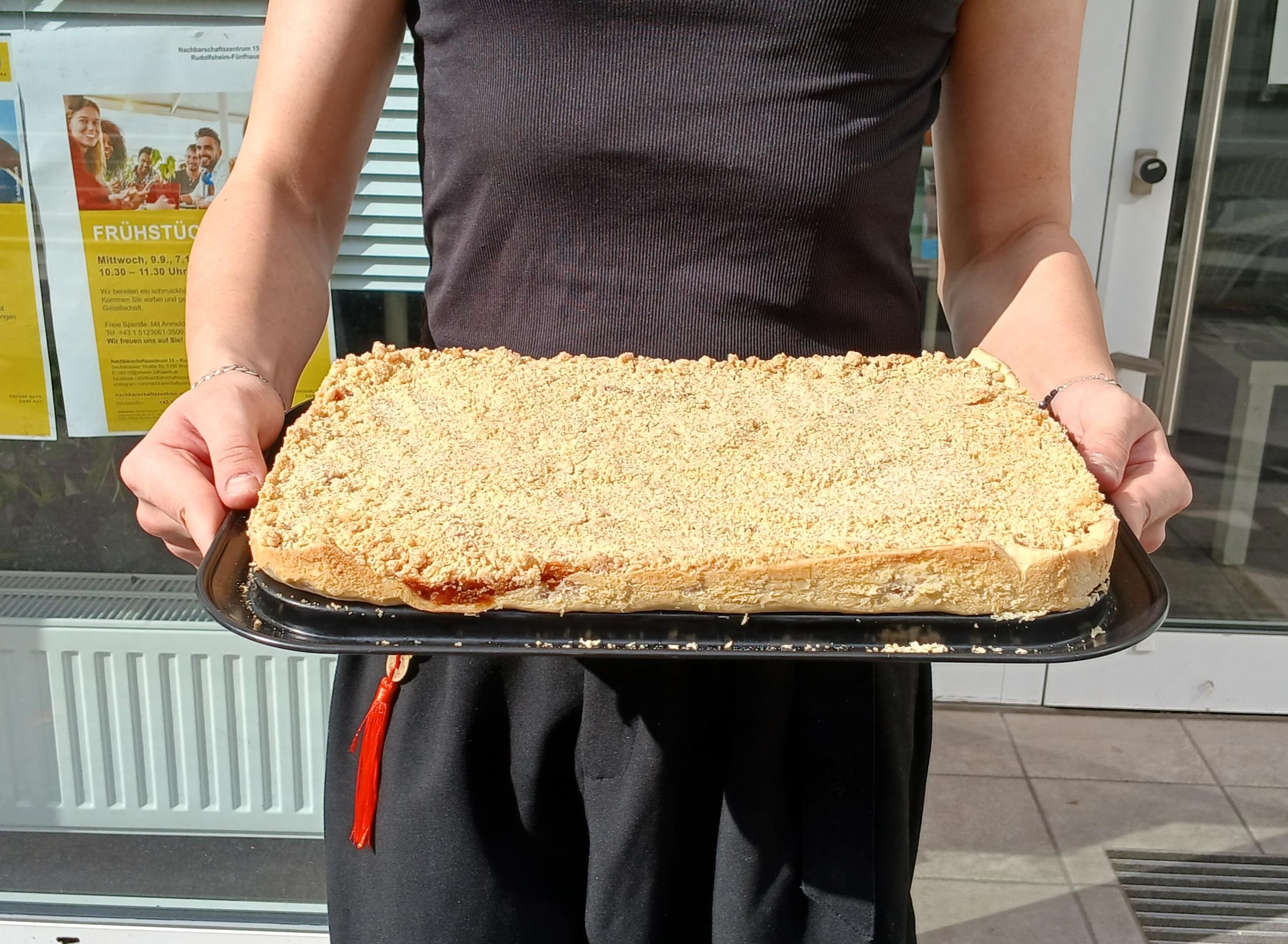 John präsentiert selbstgebackenen Apfelstreuselkuchen vor dem Sprachencafé