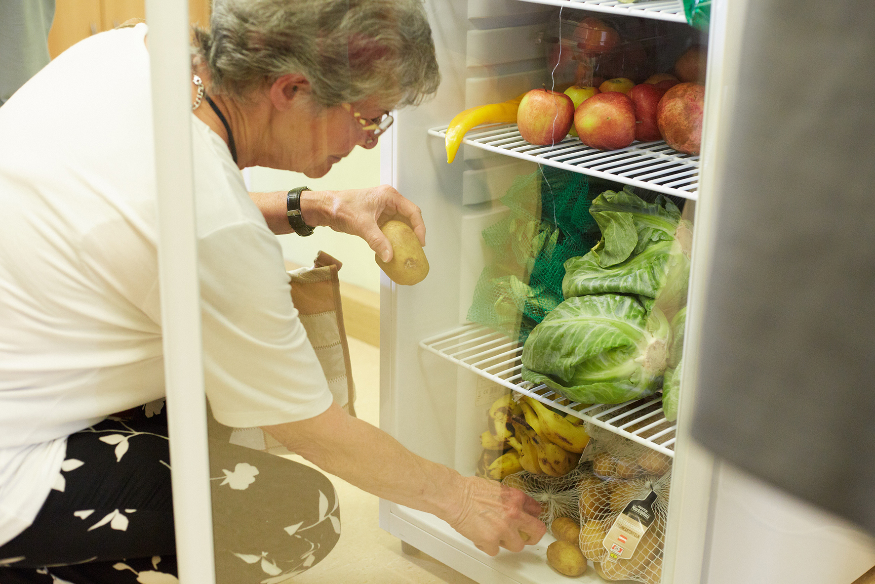 Ältere Frau nimmt Obst und Gemüse aus dem Fair-Teiler-Kühlschrank