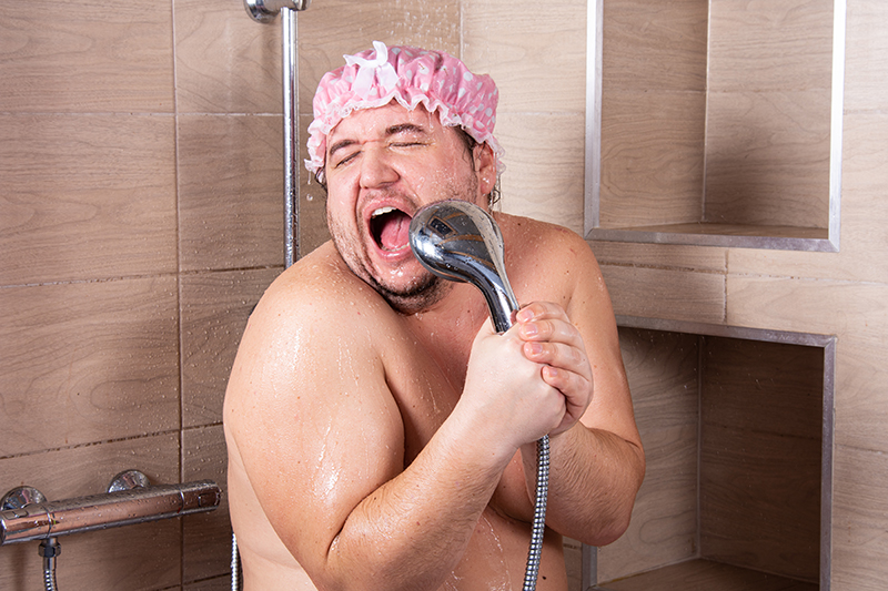 Mann singt unter der Dusche mit einem Duschkopf als Mikrofon in der Hand