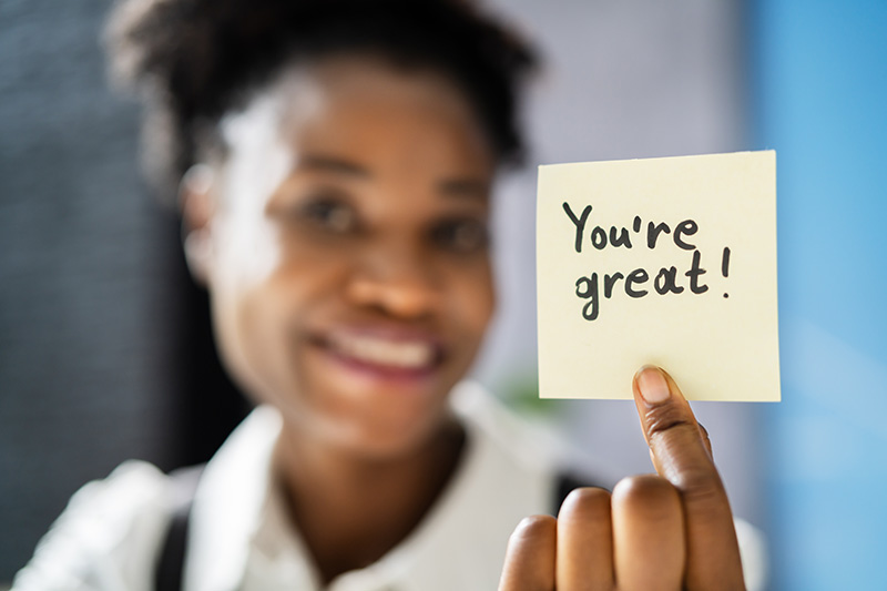 Eine Frau hält ein Post-It mit der Aufschrift „You’re great!“ in die Kamera