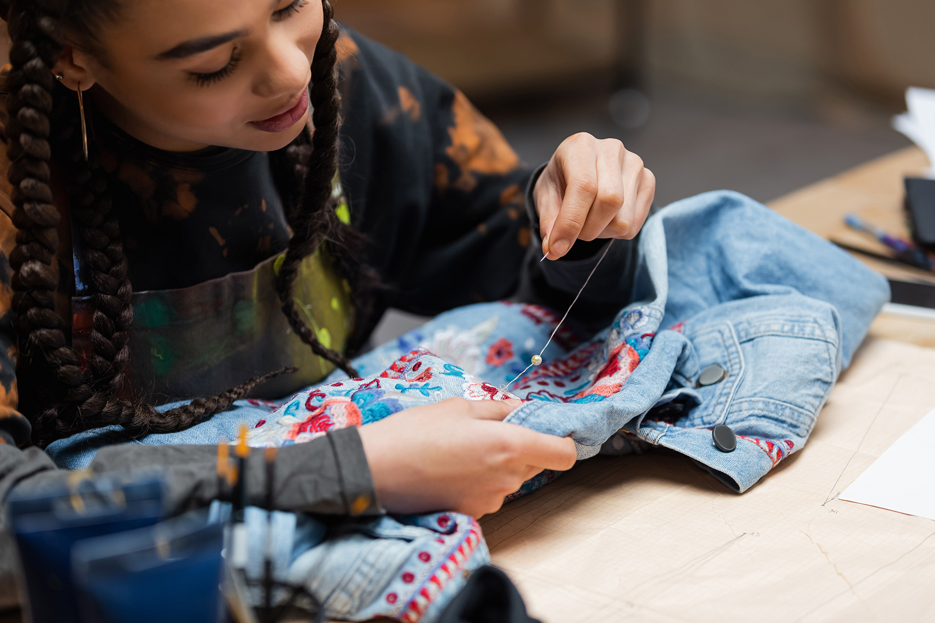 Eine junge Frau bestickt ihre Jeansjacke mit bunten Mustern.