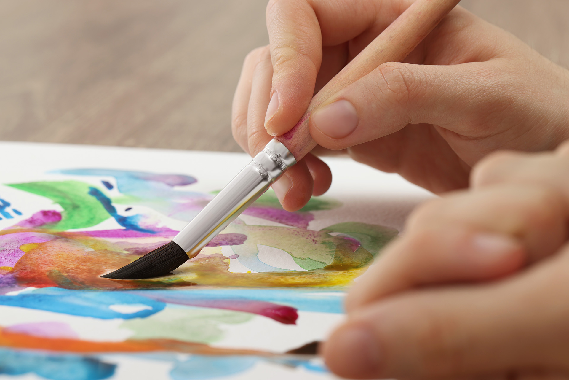Nahaufnahme einer Hand, die den Pinsel schwingt und bunte Farben aufs Papier bringt.