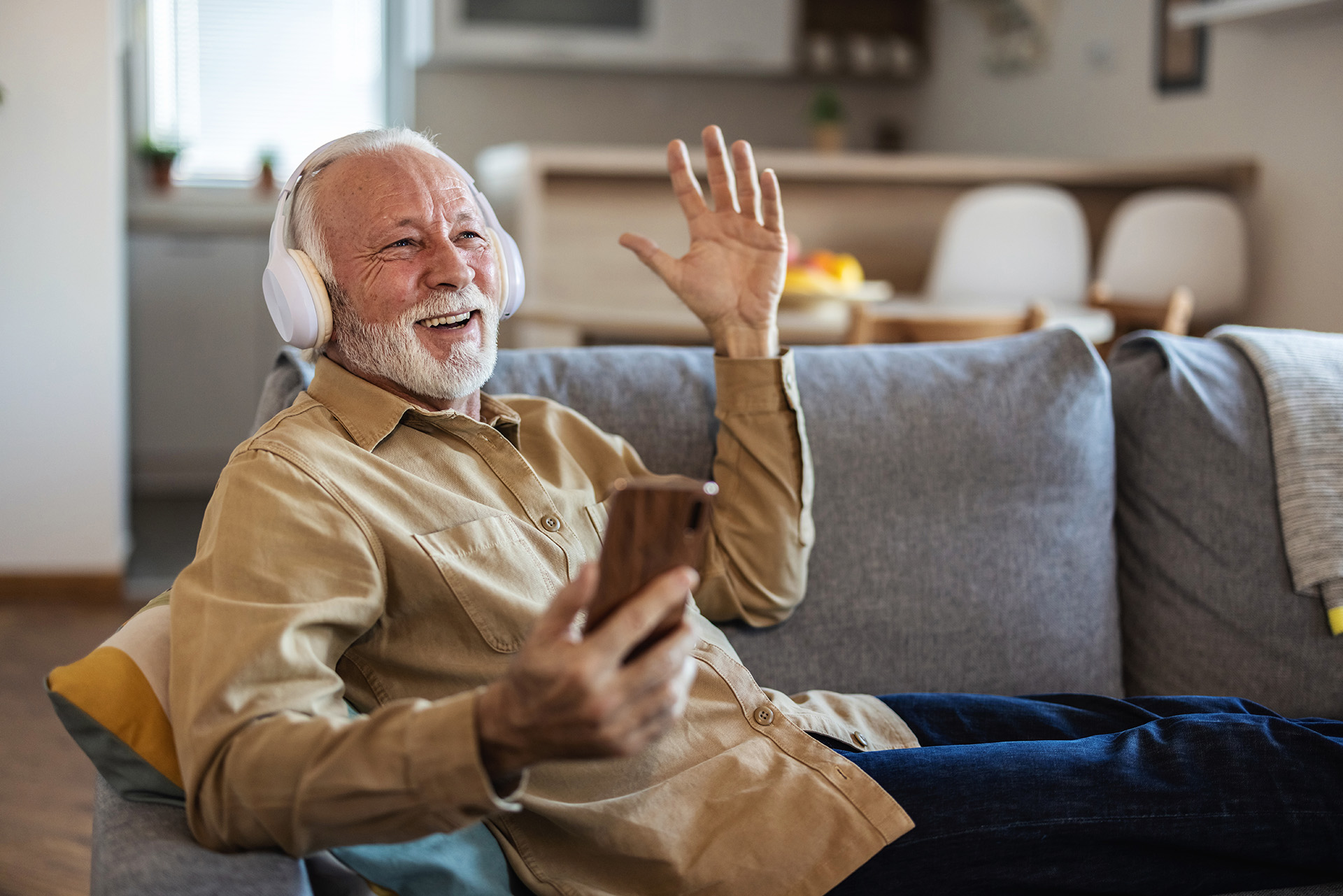 Ein älterer Mann sitzt auf der Couch und hört über Kopfhörer seinen Lieblingssong.