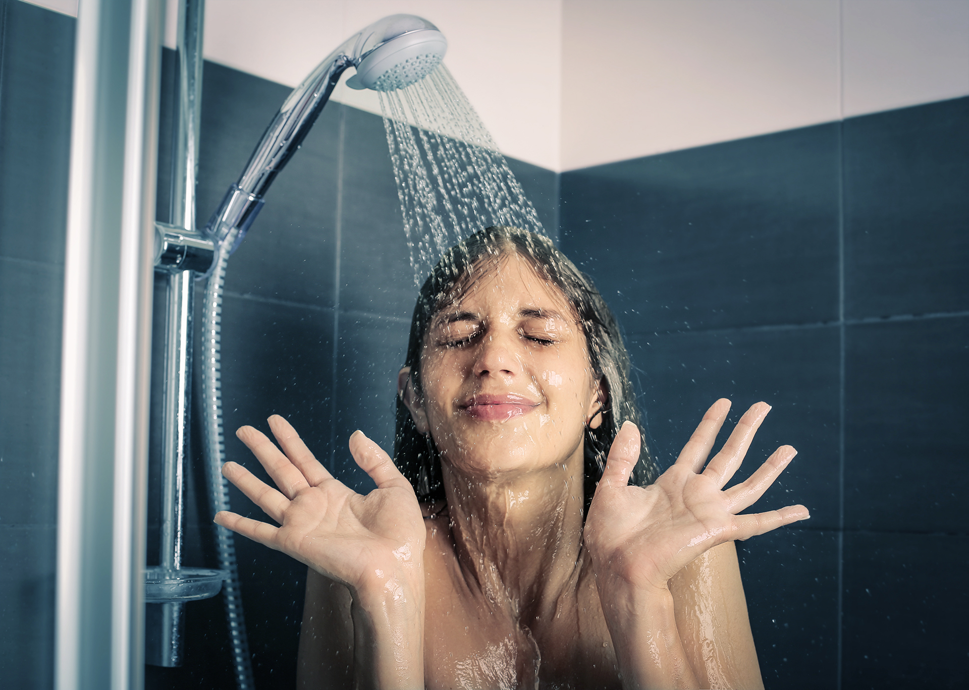 Eine junge Frau steht unter der kalten Dusche.