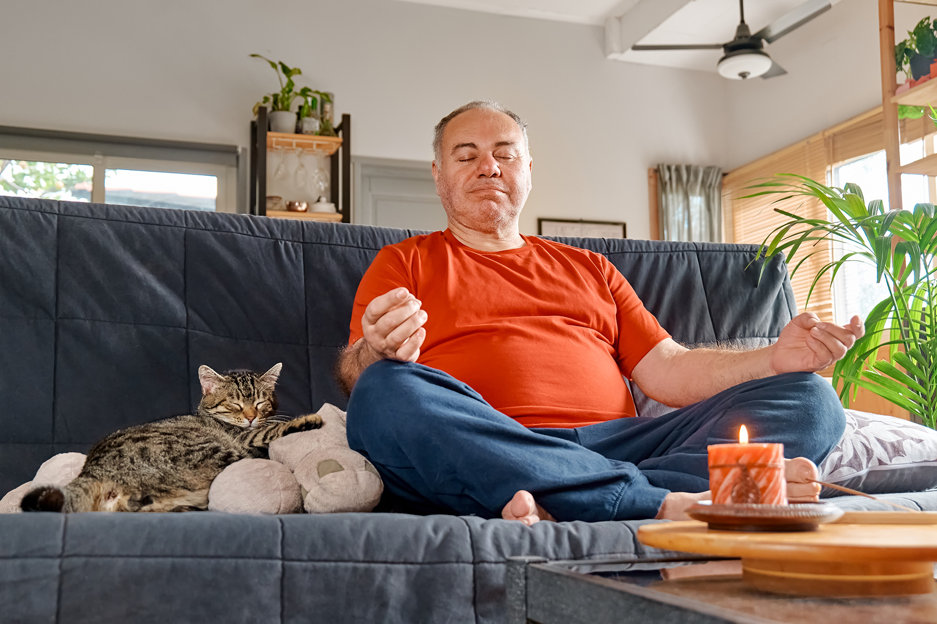 Ein Mann sitzt im Schneidersitz mit seiner Katze auf der Couch.