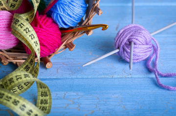 Wollknäuel unterschiedlicher Farben mit Maßband und Stricknadeln.