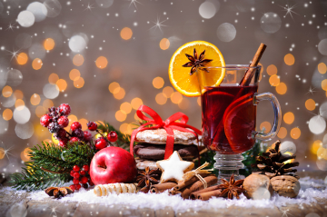 Weihnachtliches Ambiente. Punsch mit Zimtstange und Orange; Lebkuchen, Zimtstern und Apfel hinter Schneeflocken.