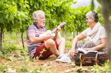 Mann und Frau sitzen im Weinberg. Mann spielt auf einer Ukulele und singt.