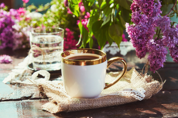 Elegante Kaffeetasse und Glas Wasser vor blumigen Ambiente.